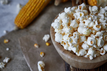 Traditional popcorn in a wooden bowl and corncobs on the table.