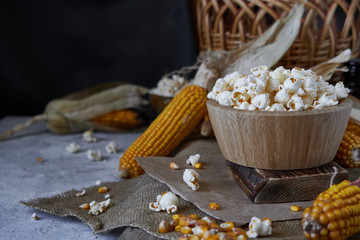 Traditional popcorn in a wooden bowl and corncobs on the table.