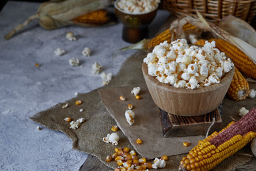 Traditional popcorn in a wooden bowl and corncobs on the table.