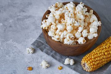 Traditional popcorn in a wooden bowl and corncobs on the table.