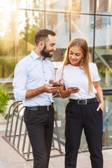 Optimistic young business couple colleagues standing near business center at the street using mobile phones.