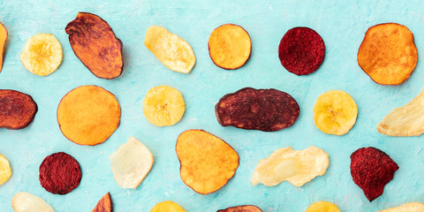A panoramic overhead shot of dry fruit and vegetable chips. Healthy vegan snack, an organic food flat lay pattern on a teal blue background