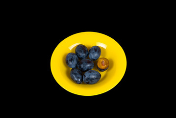 Plums on a yellow plate isolated on a black background top view