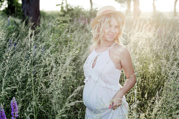 a beautiful pregnant woman stands among greenery lawn and smiles