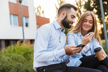 Colleagues man and woman businesspeople sit outside at the street using mobile phones.
