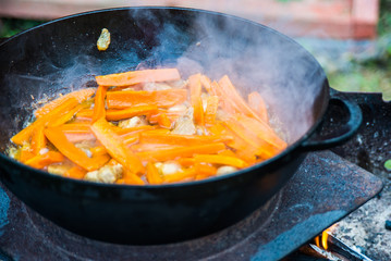 Roasted carrots with onions and meat in a cauldron. The process of cooking pilaf on the fire. Firefood