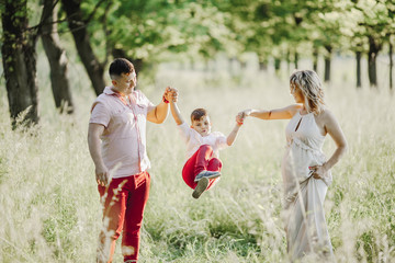 a father with a mother hold a son hands and toss him among greenery lawn