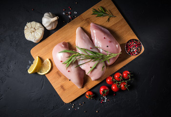 Raw chicken fillet on a wooden board on a black background