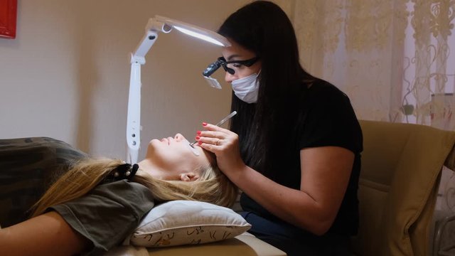 Woman Eye with Long Eyelashes. Eyelash Extension. Lashes, close up, selected focus. Gluing artificial eyelashes with tweezers. Beautician in magnifier glasses performs laborious small work.