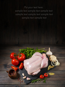 Raw chicken on a wooden board on a black background with text placeholder