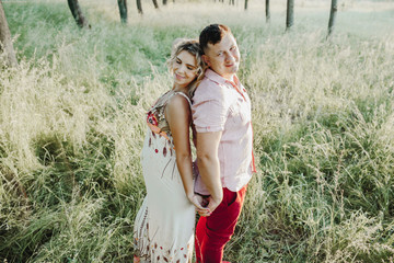 a man with his wife stand with their backs to each other and hold hands among lawn