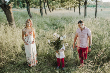 a little boy holds peonies and his parents stand on the sides on lawn