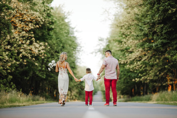 parents hold their son by hands and walking on a road