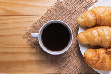 Closeup croissant with coffee on wooden table. breakfast concept.