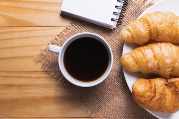 Closeup croissant with coffee on wooden table. breakfast concept.