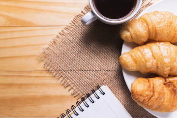 Closeup croissant with coffee on wooden table. breakfast concept.