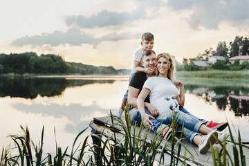 parents with their son sit on a bridge with lake view and smile