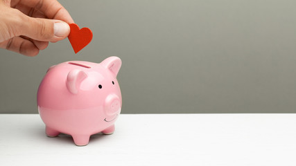 Donations of love and feelings, sympathy. Man puts heart in piggy bank. Copy space for text.