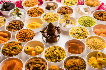 Rangoli of sweets and Farsan/snacks in bowls for Diwali with diya over white background