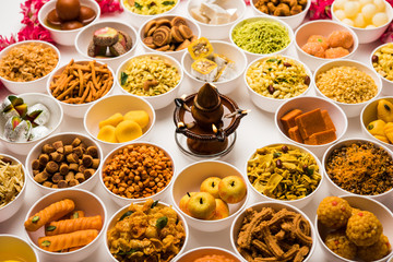 Rangoli of sweets and Farsan/snacks in bowls for Diwali with diya over white background