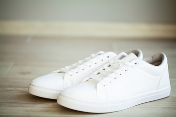 Pair of new stylish white sneakers on floor at home