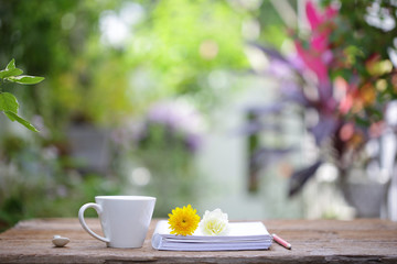 White coffee cup with yellow Chrysanthemum flowers and notebooks on wooden table at outdoor