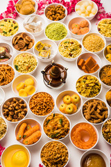 Rangoli of sweets and Farsan/snacks in bowls for Diwali with diya over white background