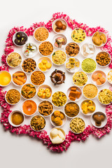 Rangoli of sweets and Farsan/snacks in bowls for Diwali with diya over white background