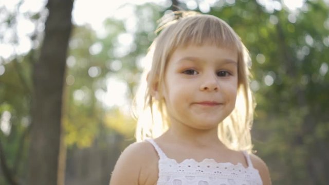 Close-up of a little cute girl looking at the camera and pointing away. Portrait of bautiful child in the park in sun rays.