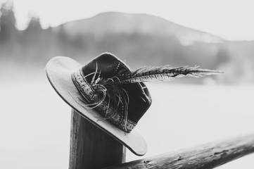 Hat with feathers handmade  on a wooden fence, a column in the winter on the background of the mountains. Close up. Black and white photo.