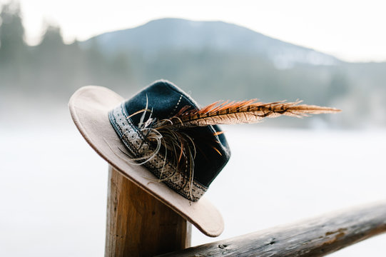 Hat with feathers handmade  on a wooden fence, a column in the winter on the background of the mountains. Close up. - Powered by Adobe