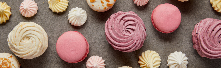 Tasty assorted small meringues, fresh soft zephyr and sweet pink macaroons on gray background