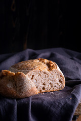 Freshly baked homemade sour dough bread on dark linen napkin, wooden background.