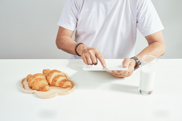 Elder man drinking milk and reading news on his digital tablet instead of newspaper