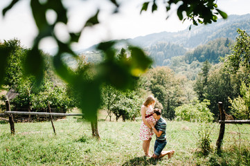 waiting baby. pregnant woman with beloved husband stand on the grass. Husband kneeling  embraces and kissing wife in a round belly. Parenthood. The sincere tender moments. mountains, forests, nature