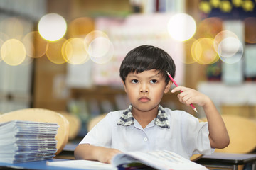An image of Asian school boy with a pencil in right hand and thinking about his practice seriously in a classroom. Young student intent on studying. Boy concentrated in the study. 