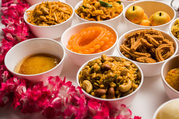 Rangoli of sweets and Farsan/snacks in bowls for Diwali with diya over white background