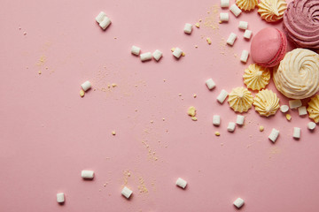 Top view of sweet pink macaroons, meringues and marshmallows with yellow pieces on pink background