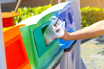 A man hand throwing a plastic glass into the green garbage bin.