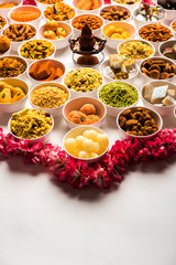 Rangoli of sweets and Farsan/snacks in bowls for Diwali with diya over white background