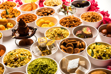 Rangoli of sweets and Farsan/snacks in bowls for Diwali with diya over white background