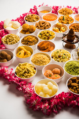 Rangoli of sweets and Farsan/snacks in bowls for Diwali with diya over white background
