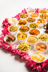 Rangoli of sweets and Farsan/snacks in bowls for Diwali with diya over white background