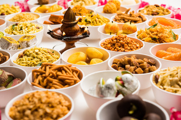 Rangoli of sweets and Farsan/snacks in bowls for Diwali with diya over white background