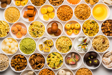 Rangoli of sweets and Farsan/snacks in bowls for Diwali with diya over white background