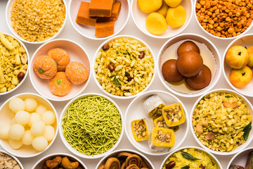 Rangoli of sweets and Farsan/snacks in bowls for Diwali with diya over white background