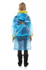 Full length back shot of a little blonde girl dressed in a blue nacre raincoat, black jeans and black high shammy boots. The raincoat with child cartoon pictures is fringed with yellow elements 