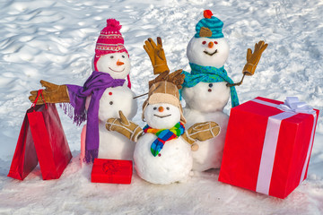Happy snowman couple and snowman child with Christmas gift standing in winter Christmas landscape. New Year greeting card. Merry Christmas and happy new year greeting card.