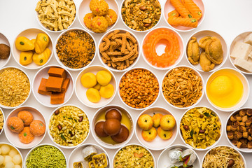 Rangoli of sweets and Farsan/snacks in bowls for Diwali with diya over white background
