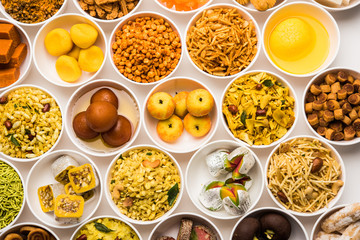 Rangoli of sweets and Farsan/snacks in bowls for Diwali with diya over white background
